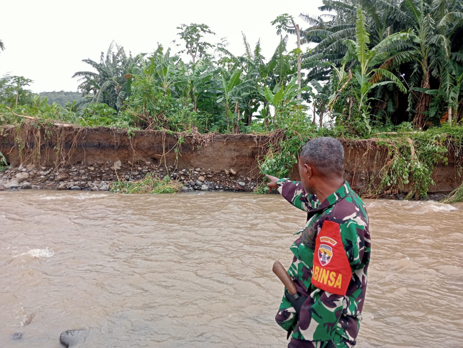 BABINSA Desa Tuleng dan Lembur Timur, Sertu. Isak Mauleti berada di tengah Kali Sungai Lembur. Mauleti sedang mengarahkan telunjuk ke arah kebun petani dan tanaman yang sebagian ludes dihantam banjir beberapa hari belakangan. Gambar diabadikan, Selasa (12/03/2024). FOTO:MW/RP